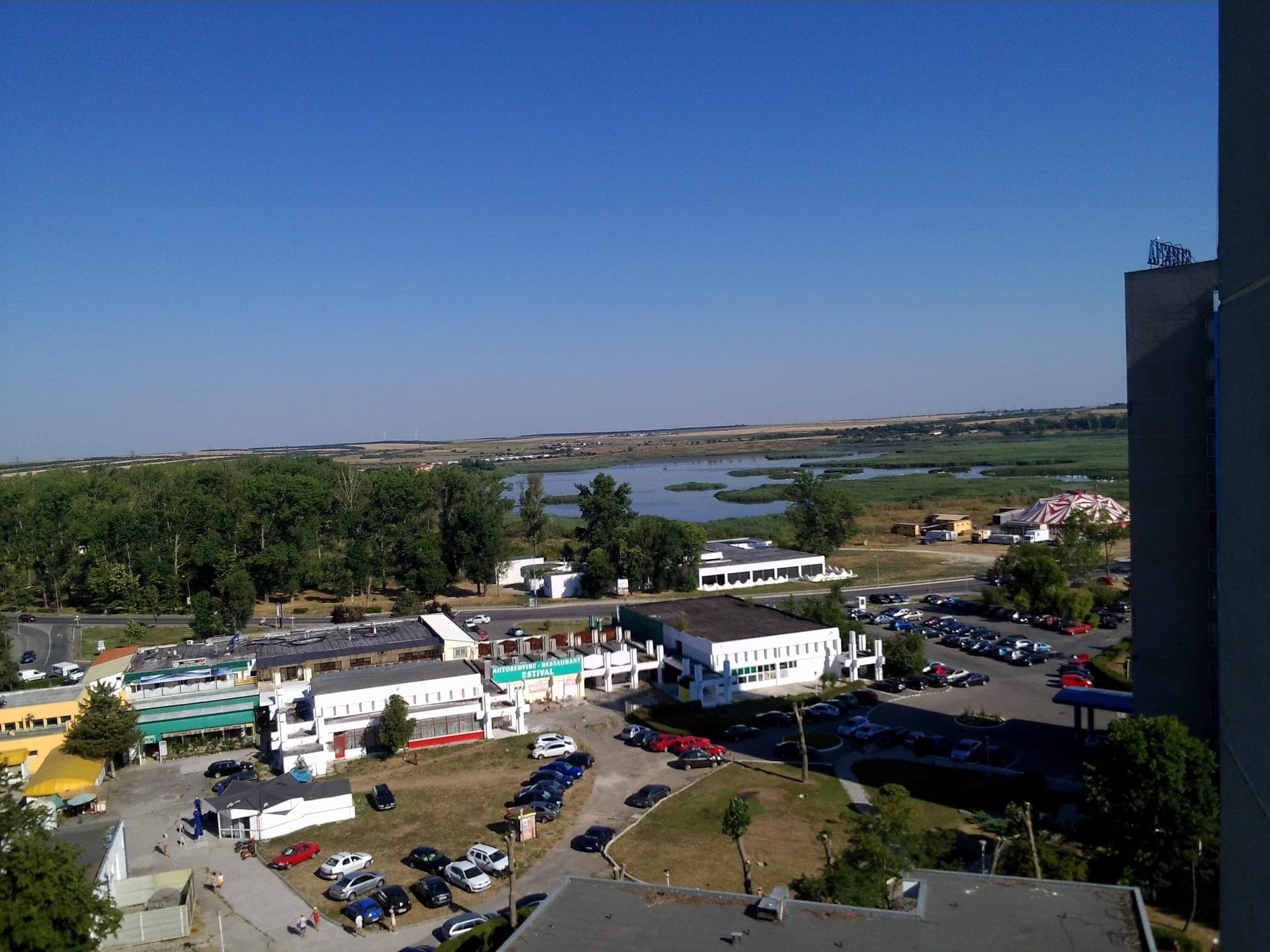 Balta văzută de sus, dintr-un hotel-turn din Saturn: ochiuri de apă albastră între insule de stuf, cu dealurile Dobrogei în spate și clădirile stațiunii în prim-plan