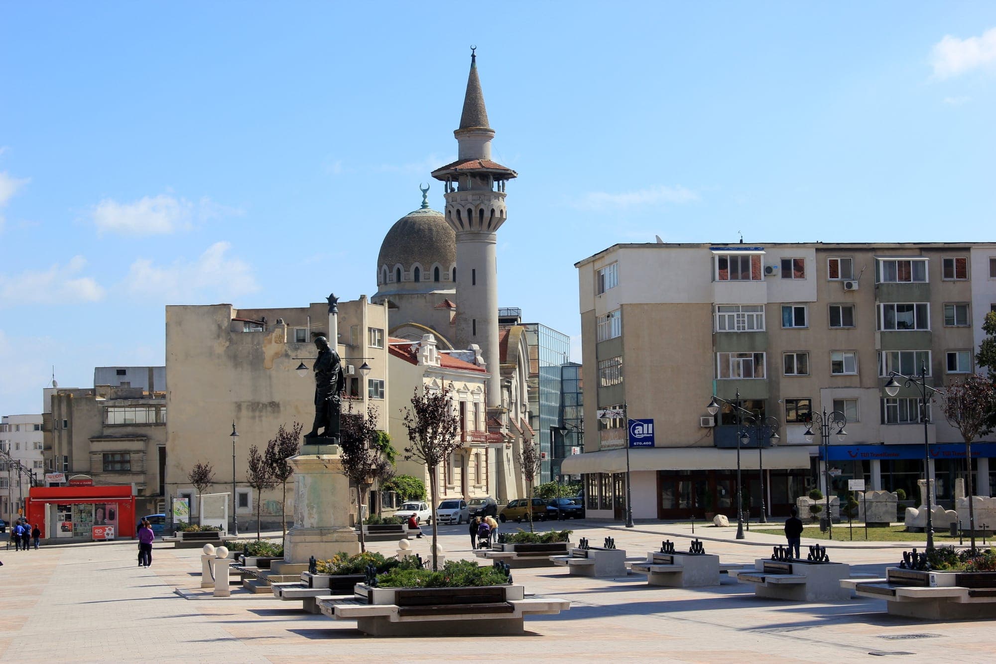 Piața Ovidiu cu statuia poetului pe soclu, bănci de piatră și minaretul Moscheii Carol I deasupra caselor